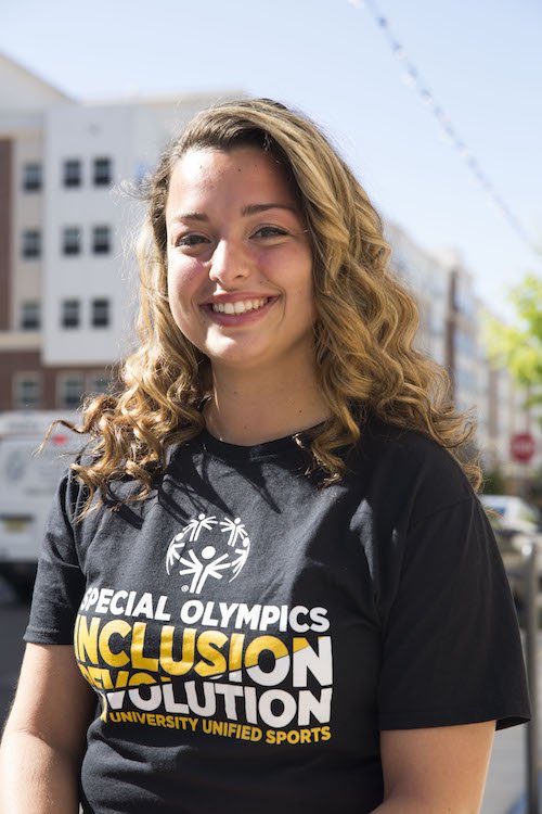 Callie DeMaria of Rowan University stands at Rowan Boulevard with buildings behind her, while wearing a black t-shirt about Inclusion