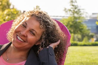 Woman sitting in pink lawn chair laughing while the sun shines down