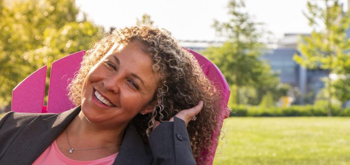 Woman sitting in pink lawn chair laughing while the sun shines down
