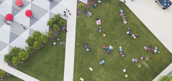 Aerial view of multiple people sitting in lawn chairs in a grassy town square