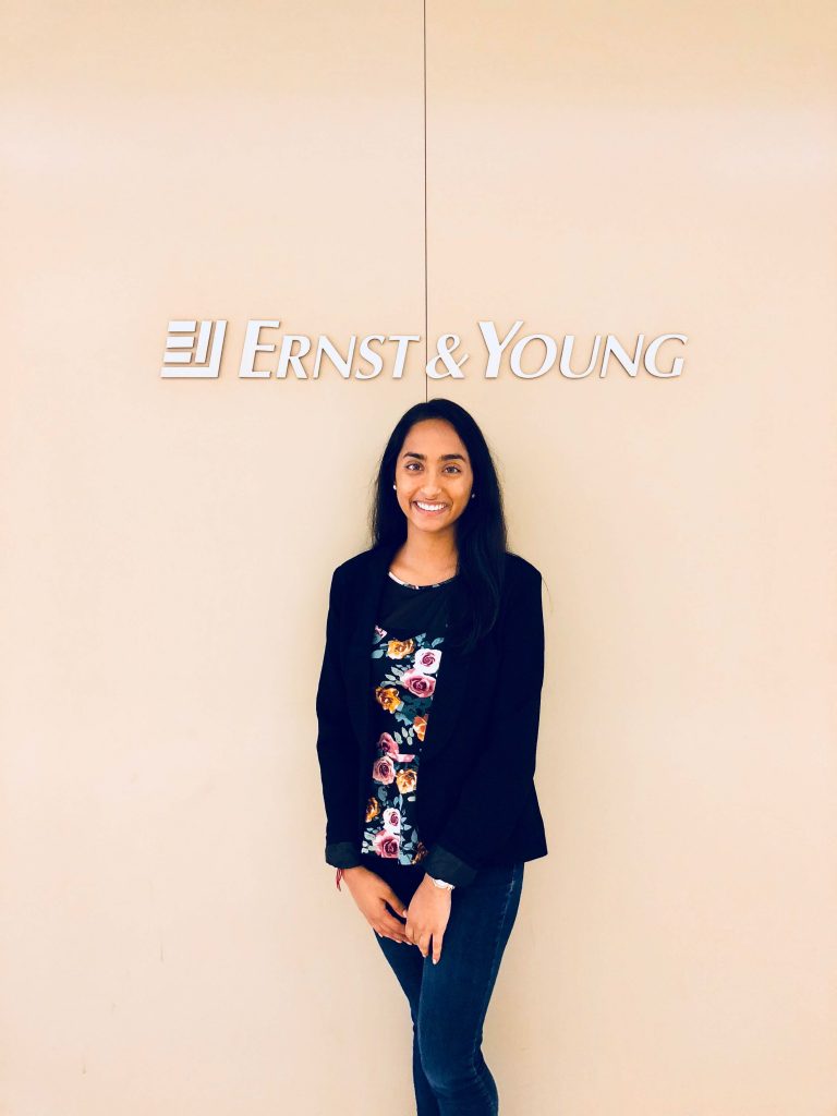 Young lady wearing a black jacket and jeans standing under a Earnest & Young Accounting Firm sign