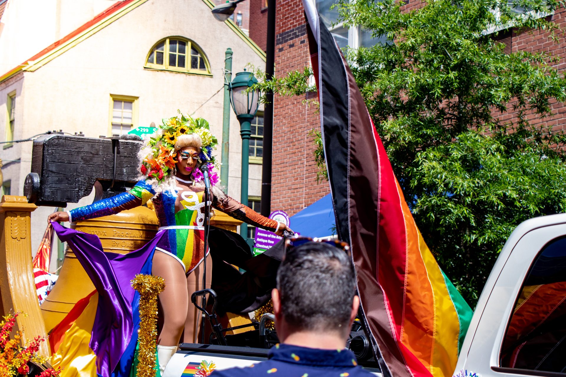 A drag queen dressed in a rainbow leotard and flowers throughout her hair