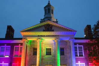 The front of Bunce Hall being lit up at night with rainbow colored lights