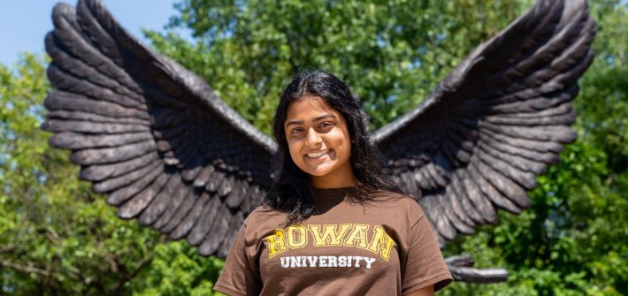 Krishna stands at Rowan University posed with the owl mascot's wings behind her