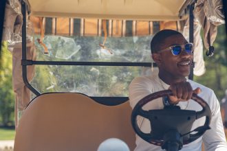 Silas sits in the driver's seat of a Rowan golf cart with one hand on the wheel, looking off camera