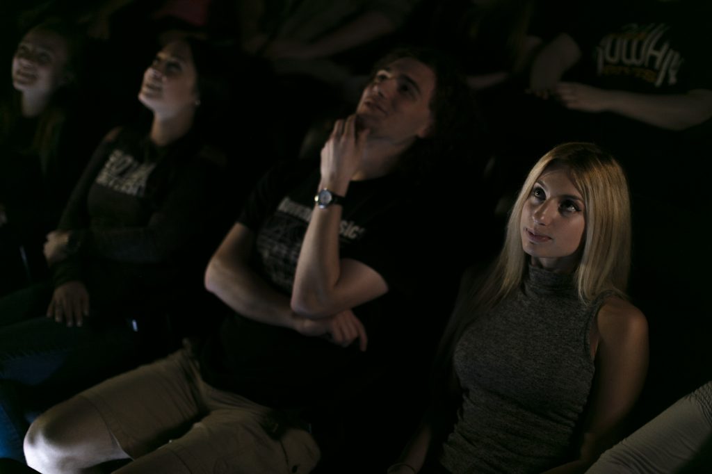 a row of student sit at the Rowan University planetarium, looking up at a presentation