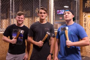 Three male students stand holding axes