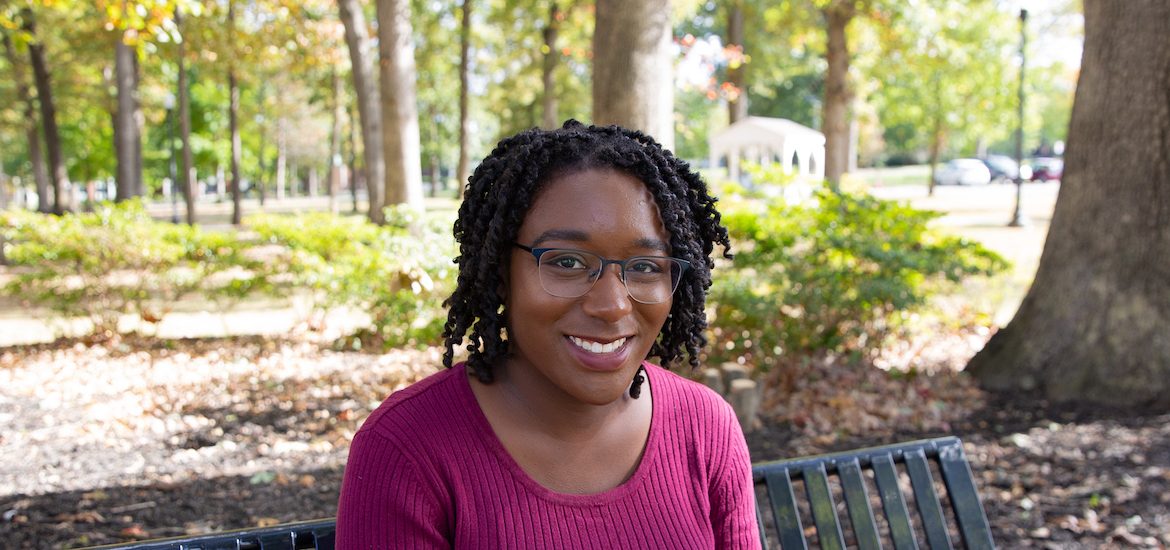 Jessica Hassell, a Higher Education Administration track graduate student and author of story, sits in woods on Rowan University's campus