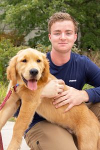 Piano Performance major Ben holds Zazu, a golden retriever puppy, in his lap outside