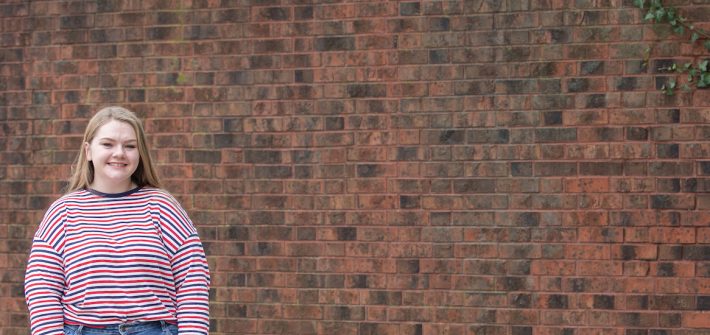 cassidy stands in front of a brick wall.