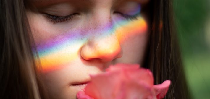 A close up photo of a girl holding a rose to her face.