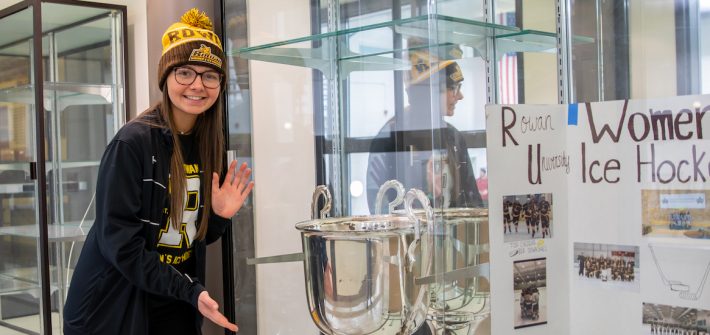 Emily stands in front of the women's ice hockey trophy.