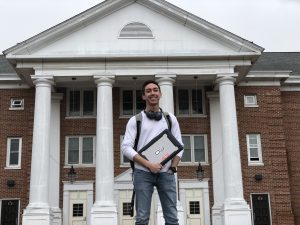 ,JT poses in front of Chestnut Hall with his laptop and headphones.