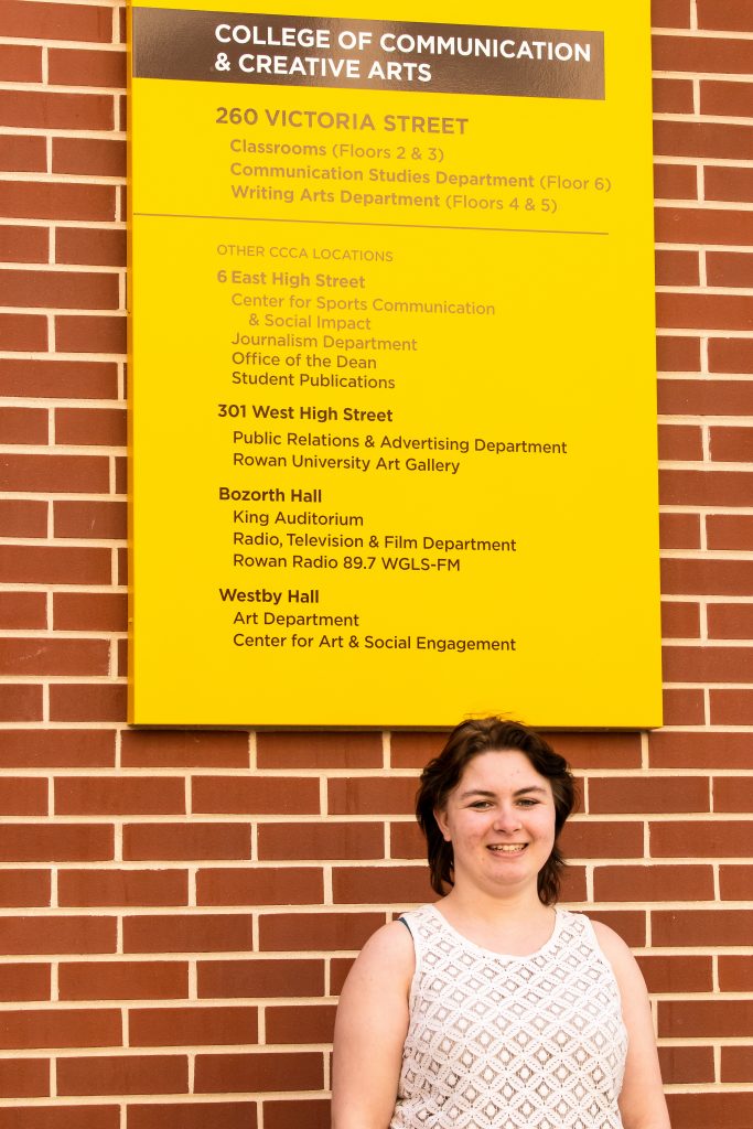 Marissa stands below a sign for the communications building.