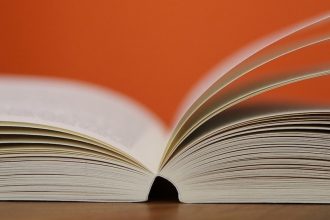 Stock image of an open book fanned against an orange background.
