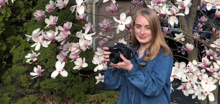 Nicole stands in front of a magnolia tree with a camera.