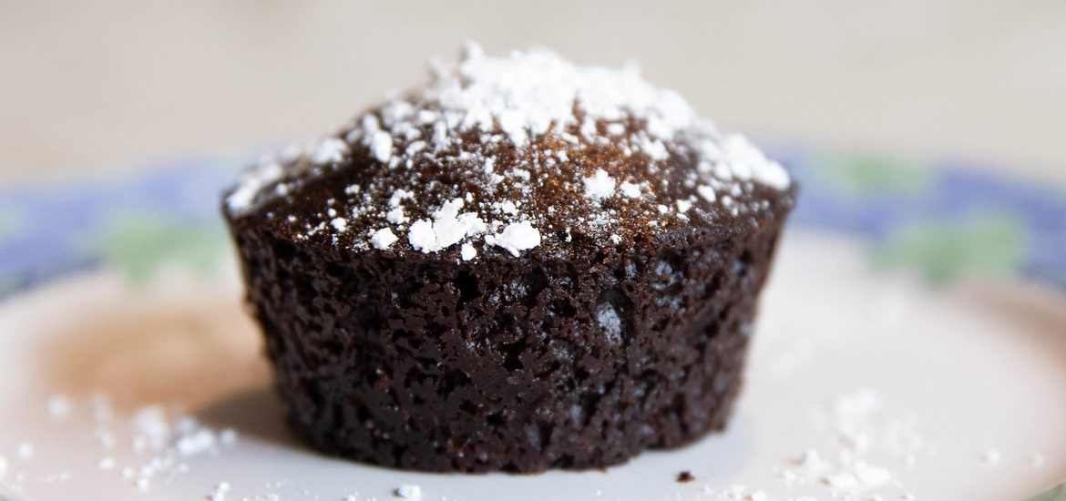 A chocolate cupcake with powdered sugar on top on a plate.