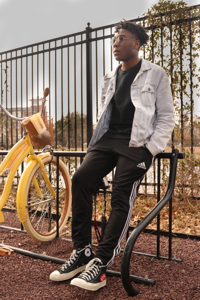 Jelani leans against a fence, hands in his pockets, with bikes next to him.
