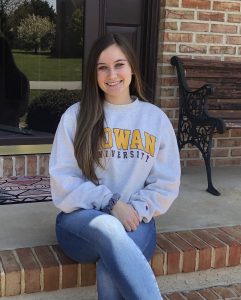 College of Business student Christina wears a Rowan sweatshirt and sits on the front porch of her home.