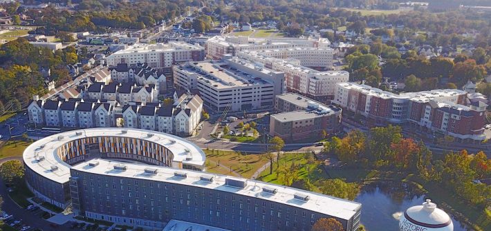 Drone view of Holly Pointe curved building with trees in the horizon.