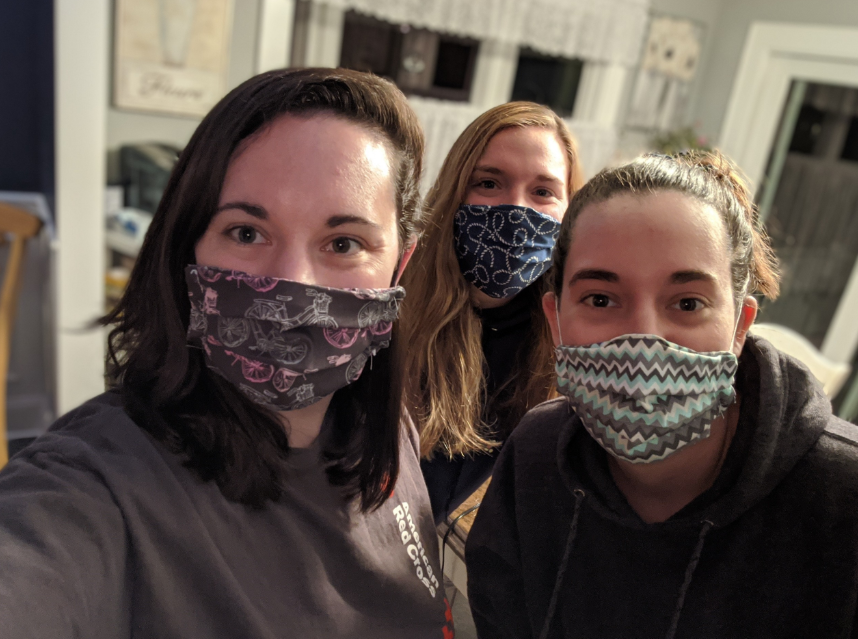 Brittney and her two sisters stand with mouths covered by homemade masks.