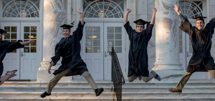 4 rowan grads jump in graduation attire.