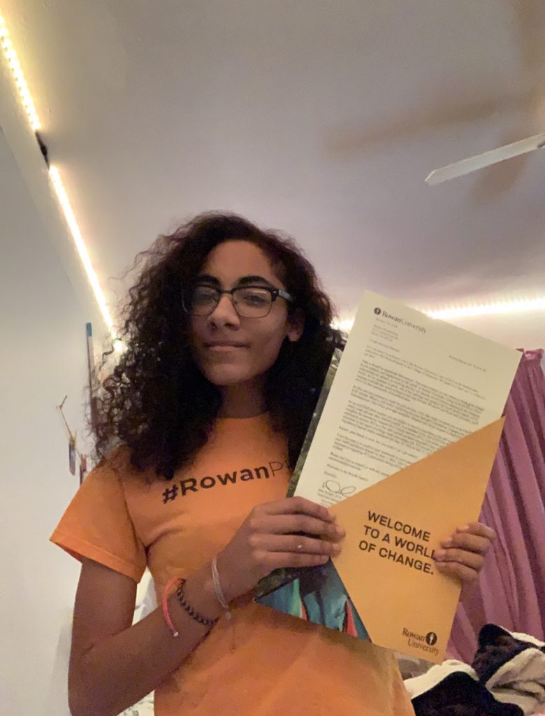 Rachel Bonhomme is wearing a #RowanPROUD T-shirt and is holding up her acceptance letter.