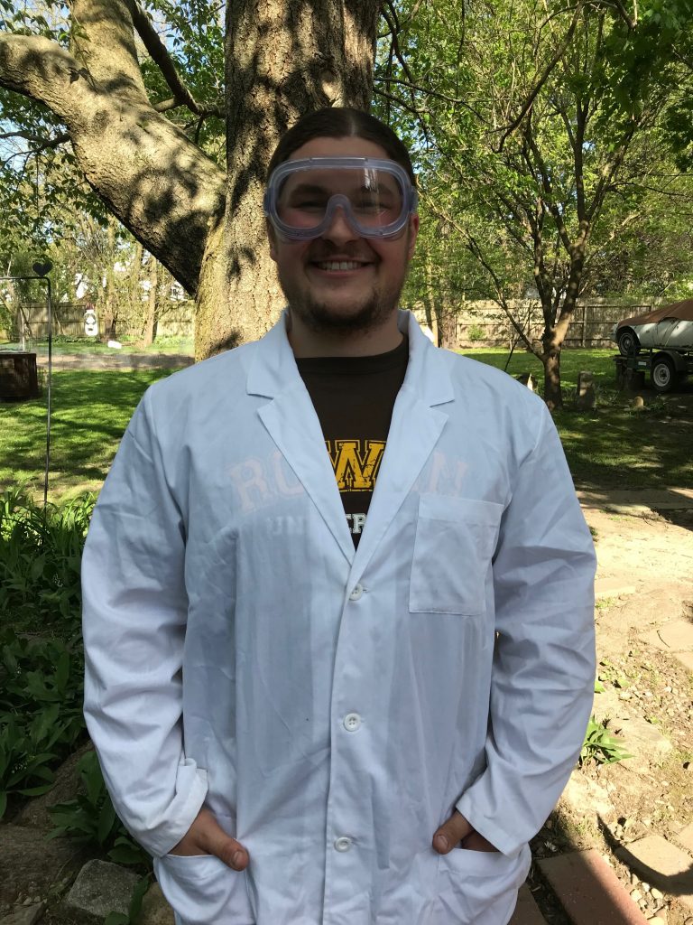 Jacob Emig stands outside wearing goggles and a white lab coat.