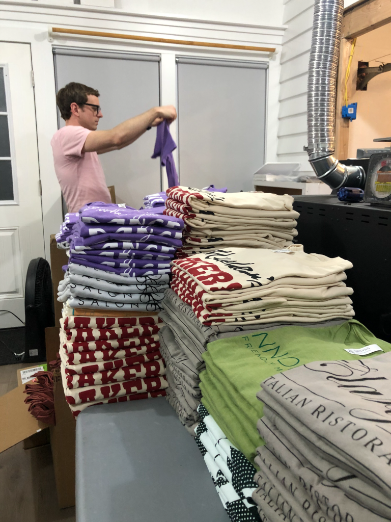 Justin folds a stack of purple t-shirts at Wider Awake.