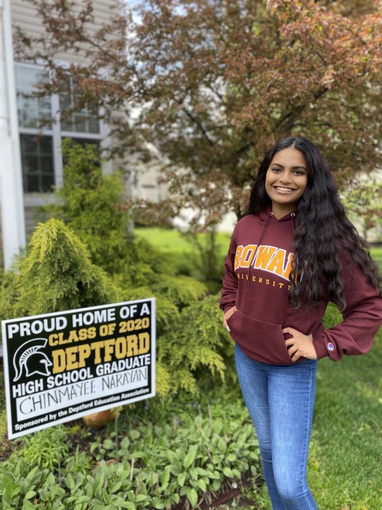 Chinmayee stands in front of a high school graduation sign, wearing a Rowan shirt.