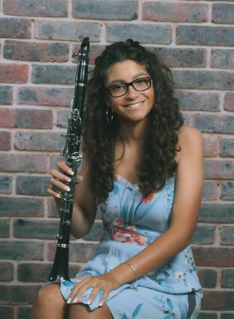 a portrait of Antonietta sitting in front of a brick wall and holding her clarinet.