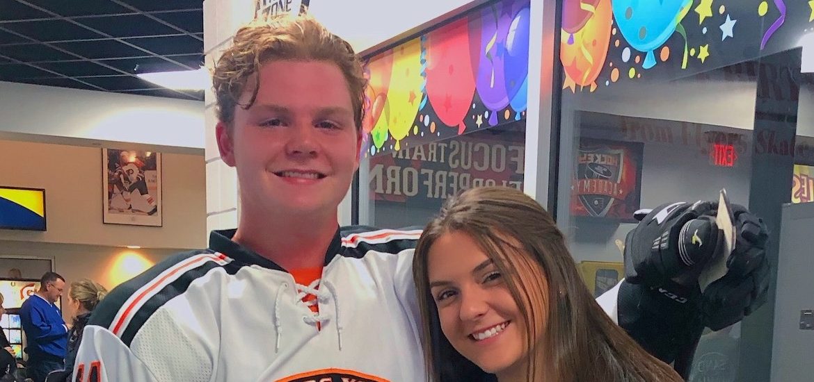 A close up of George wearing an ice hockey uniform, standing close to a young woman.