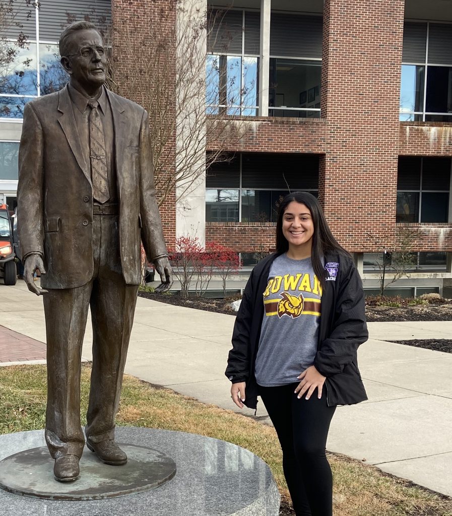 Maria stands in front of a statue of Henry Rowan at Rowan University.