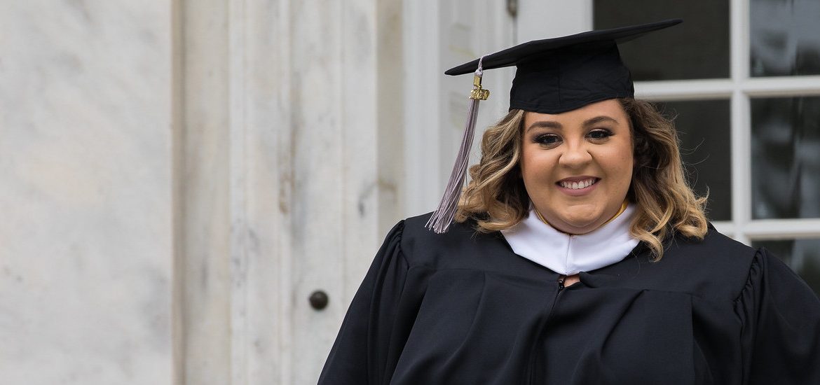 Megan Pfizenmayer stands outside of Bunce Hall in her cap and gown