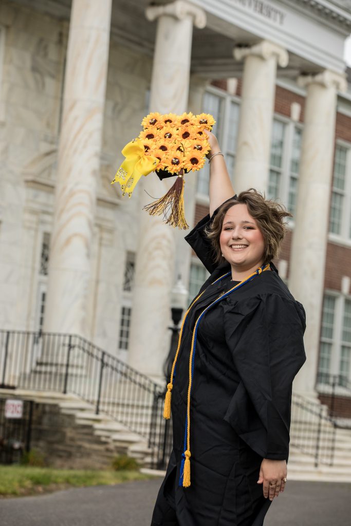 Chelsey holds up her decorated sunflower cap in front of Bunce Hall