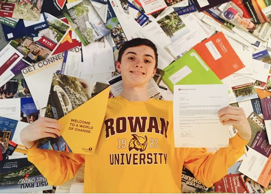 Danny holding up his acceptance letter from Rowan while laying on a pile of University pamphlets.