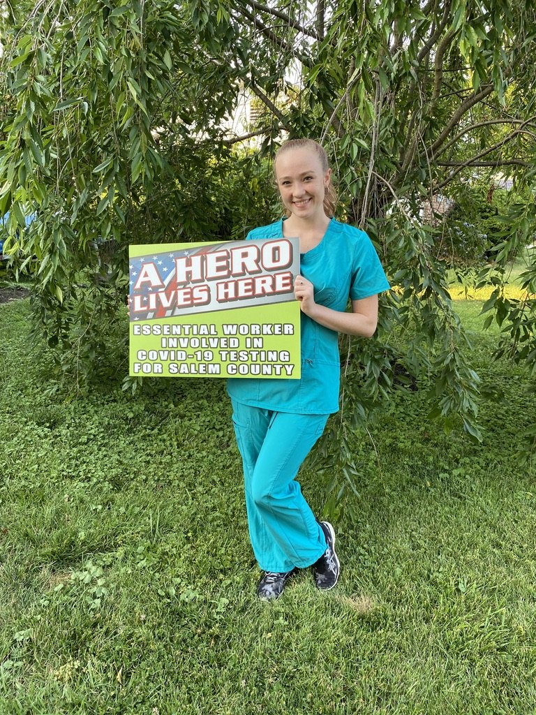 Katelyn poses in her scrubs with a sign that says "A Hero Lives Here".