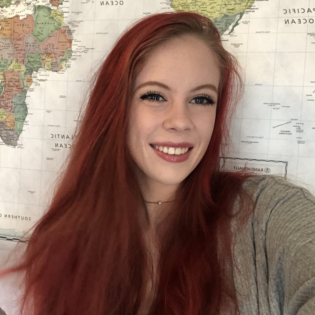 Julia smiling and posing for a selfie in front of a world map.