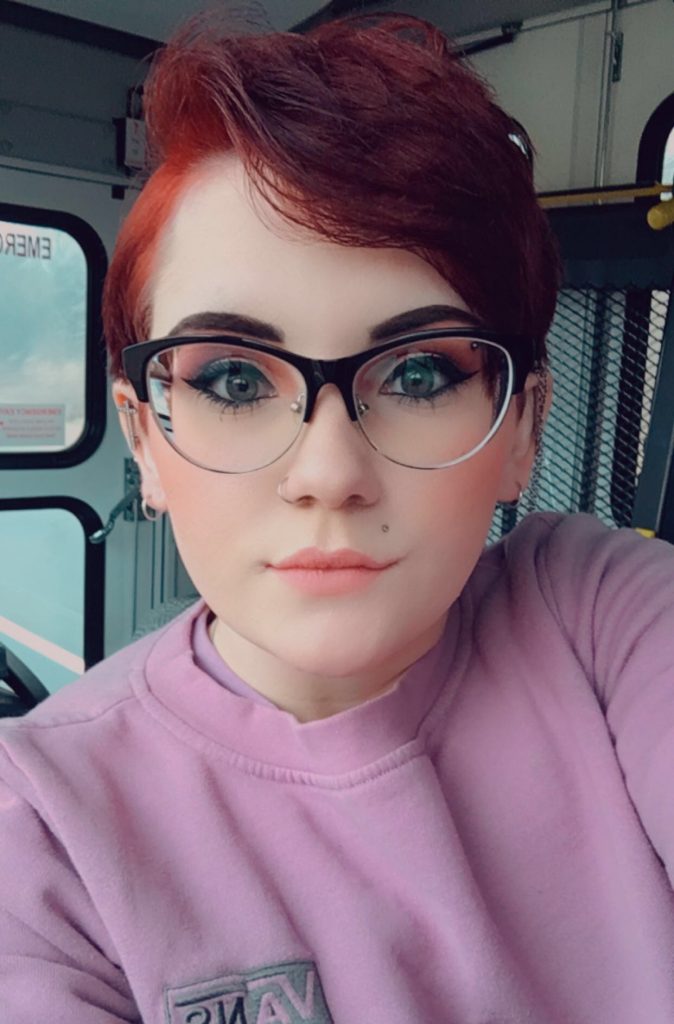 Diana posing for a selfie wearing glasses and a pink sweatshirt. 