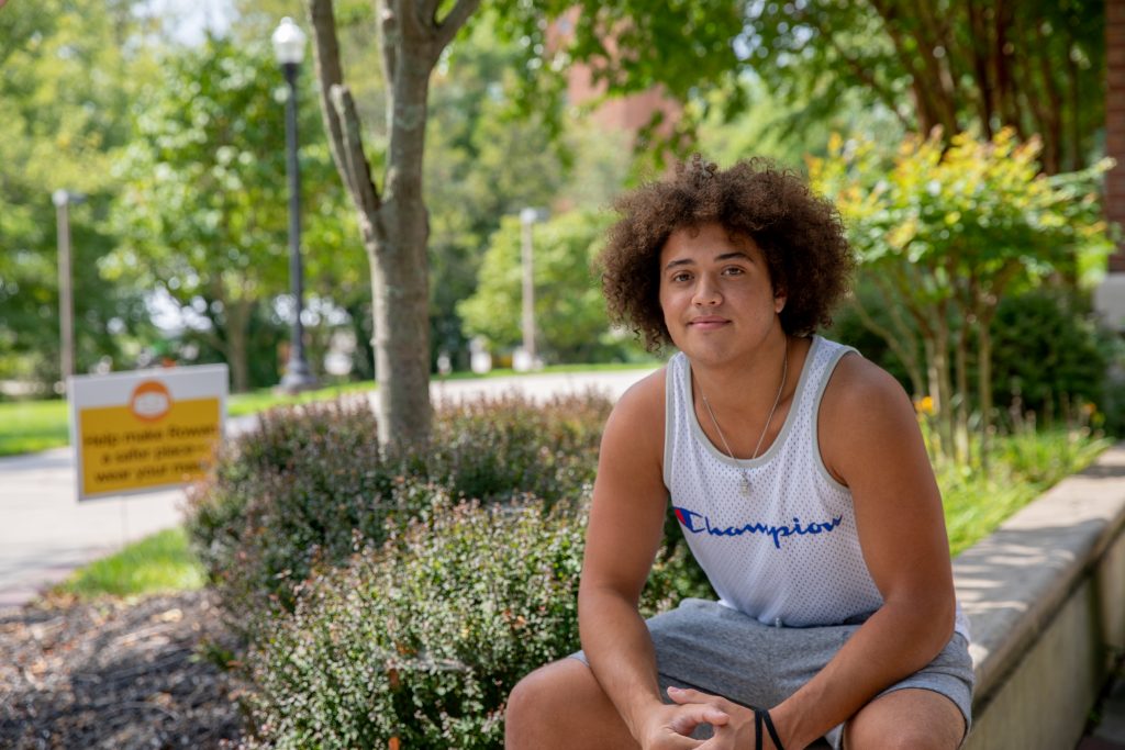Jalen sitting and smiling on the edge of Mimosa hall.