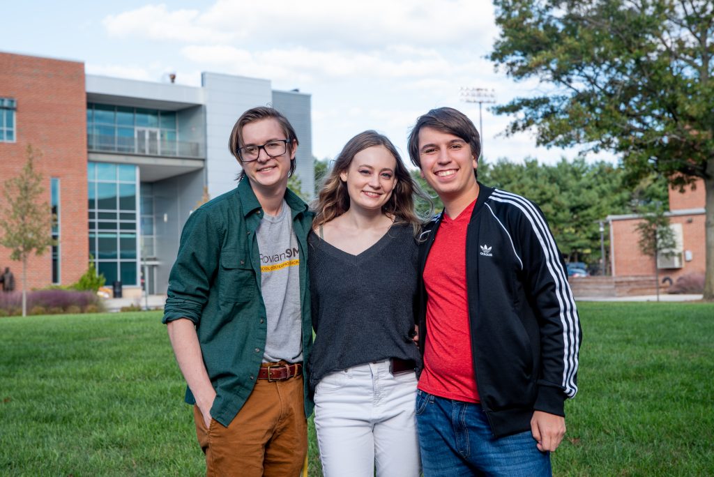 Alex and her two friends standing outside on a field with James Hall in the background. 