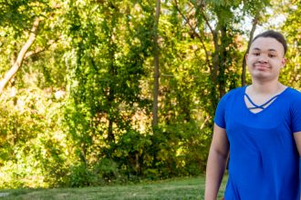 Christine standing outside in front of trees in a blue shirt.