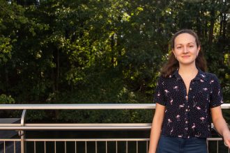 Jennifer stands outside by a wooded area of campus.