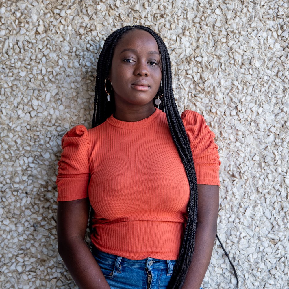 Nafisat Olapade poses in an orange shirt in front of a rocky wall.