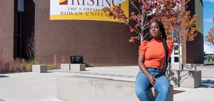 Nafisat Olapade sitting on a cement bench in front of a large brick building.