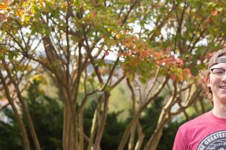 Griffin poses in a backwards hat in front of orange and green trees.