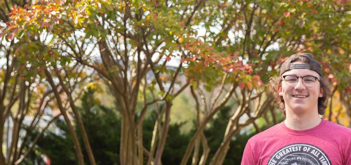 Griffin poses in a backwards hat in front of orange and green trees.