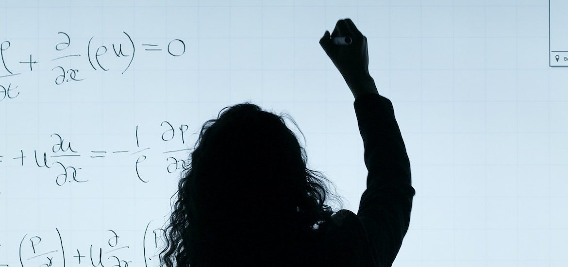 Backlit image of woman writing on a white board.