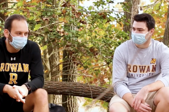Two students in Rowan gear sit at the nature preserve.