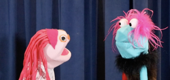 Two puppet in front of a blue backdrop.